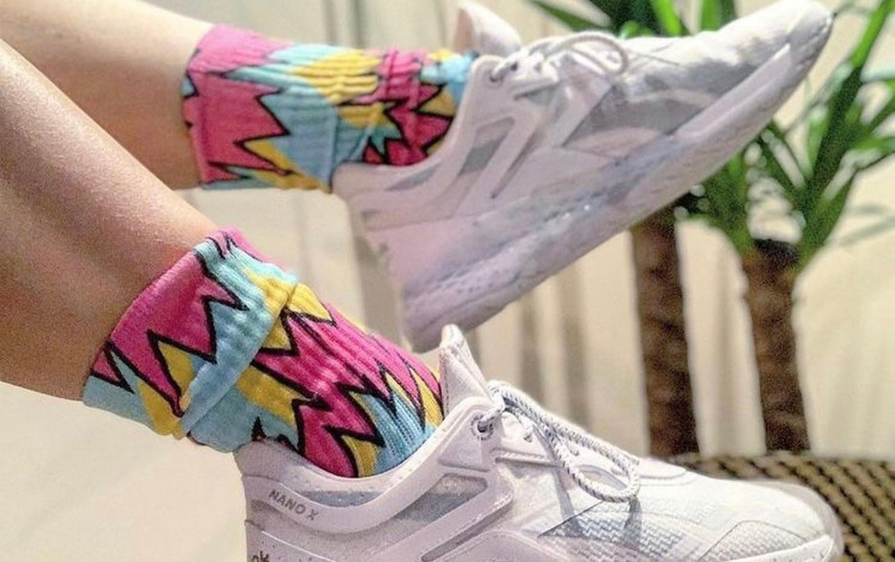 White sneakers with colorful zigzag-patterned socks on a blurred indoor background