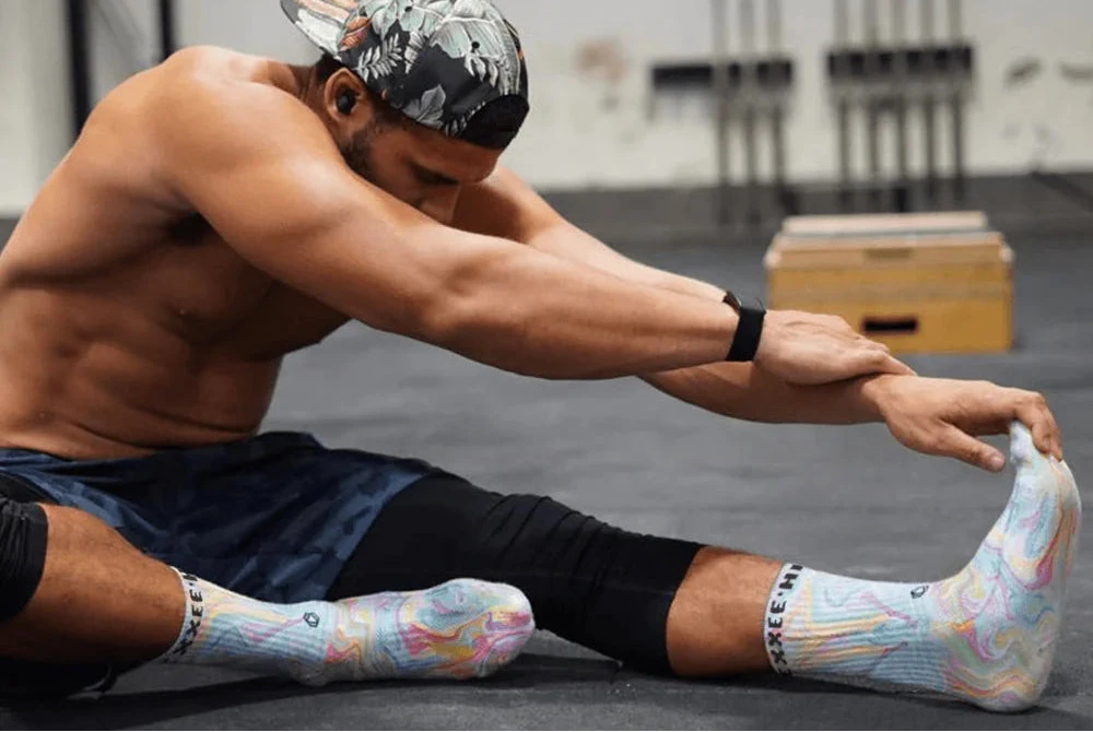 Man stretching in a gym wearing colorful socks and a bandana.